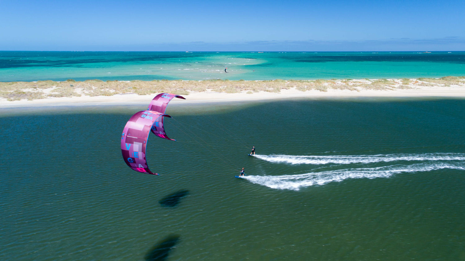 Two kitesurfers riding side by side with a pink kite in the flat, shallow lagoon at Safety Bay, Perth.
